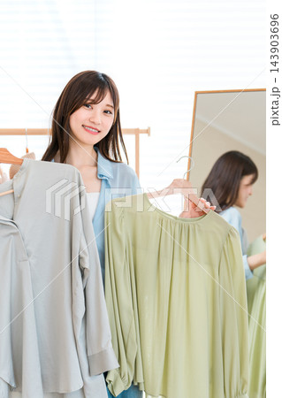 家の鏡のそばで二着の洋服を持って微笑む若い女性。 143903696