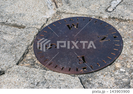 Nitra, Slovakia - May 29, 2024: Round metal compass marker set in cracked stone 143903900