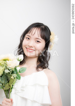 [白背景]白いウェディングドレスを着てブーケを持つカメラ目線の若い20代の日本人女性の花嫁 143905082