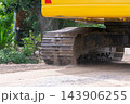 The steel track of yellow excavator rests sandy ground layered tread plates rollers dark soil marks visible beneath the machine body close view of construction equipment 143906255