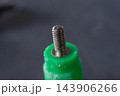 A silver threaded metal stud rises from green plastic fitting worn edges surface marks against softly blurred dark gray background detailed close view of hardware part 143906266