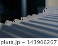 A row of white metal panels has bent mounting tabs round holes shadows repeating across the surface against dark background close view of industrial equipment components 143906267