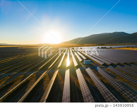Solar panels in a field at sunset near mountains and water in a rural area 143910958