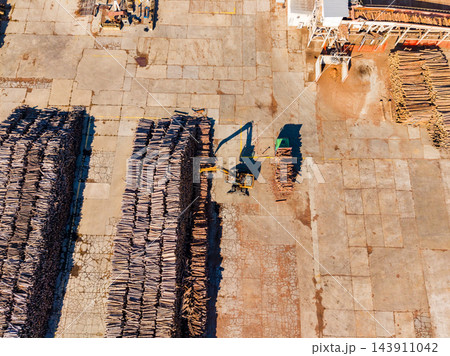 Aerial view of a forklift moving timber stacks across a paved lumber yard during daytime 143911042