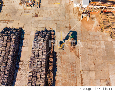 Aerial view of a forklift moving timber stacks across a paved lumber yard during daytime 143911044