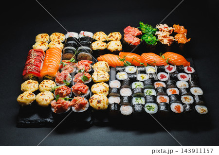 Assorted sushi rolls and nigiri arranged on a black serving tray against a dark background Assorted sushi rolls and nigiri arranged on a black serving tray against a dark background 143911157