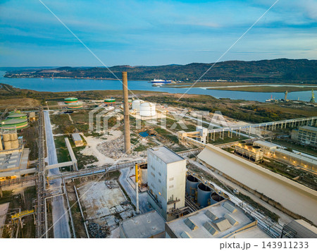 Industrial plant with tanks and processing buildings beside a coastal inlet under a daytime sky Industrial plant with tanks and processing buildings beside a coastal inlet under a daytime sky 143911233