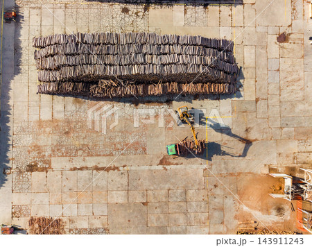 Overhead view of a construction machine moving materials across a paved work site in late afternoon light 143911243