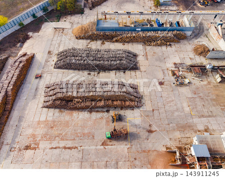 Aerial view of logs stacked in rows across a timber yard with loaders and storage buildings 143911245