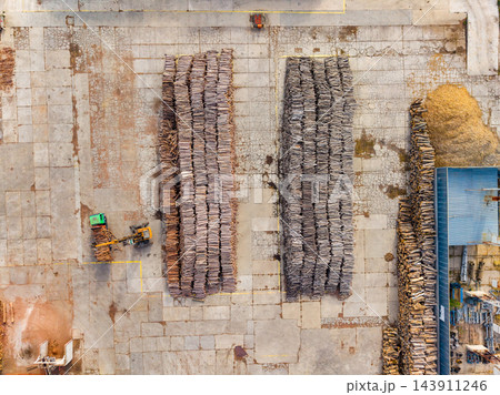 Aerial view of a timber yard with stacked logs beside a blue-roofed work area Aerial view of a timber yard with stacked logs beside a blue-roofed work area 143911246