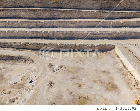 Terraced quarry excavation with haul roads and exposed layers of earth across the work site 143911302