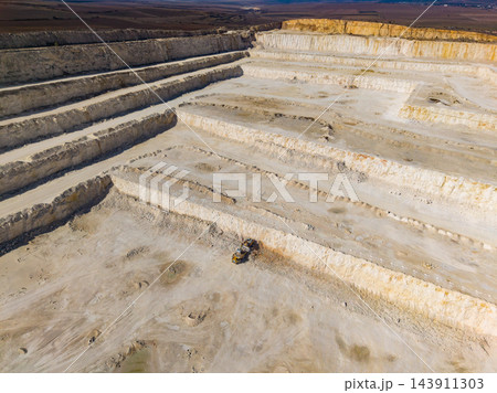 Quarry workers operate an excavator across stepped excavation benches during a daytime work shift Quarry workers operate an excavator across stepped excavation benches during a daytime work shift 143911303