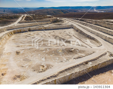Terraced quarry with haul roads and exposed rock across an open site in a rural landscape during daylight Terraced quarry with haul roads and exposed rock across an open site in a rural landscape during daylight 143911304