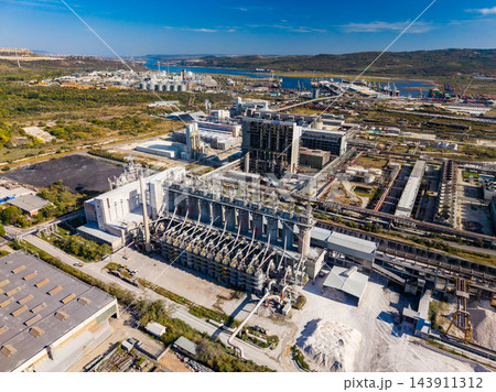 Aerial view of an industrial processing plant with buildings and equipment beside a coastal harbor during the day 143911312
