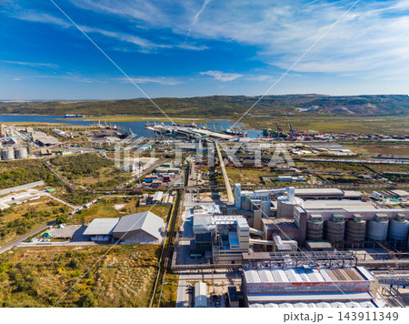 Industrial plant and port facilities along the coast near a low range of hills under a wide sky 143911349
