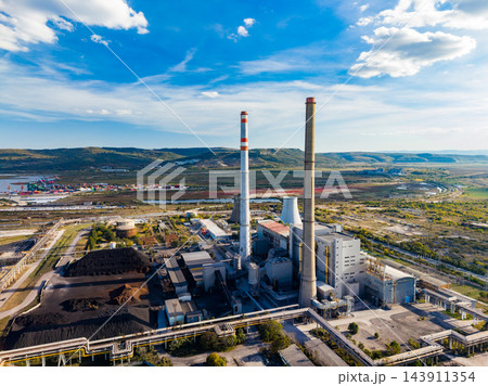 Power plant with two chimneys and industrial equipment in a broad valley under a cloudy sky Power plant with two chimneys and industrial equipment in a broad valley under a cloudy sky 143911354