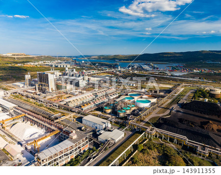 Industrial processing complex with tanks, pipelines, and buildings beside a coastal inlet under a blue sky Industrial processing complex with tanks, pipelines, and buildings beside a coastal inlet under a blue sky 143911355