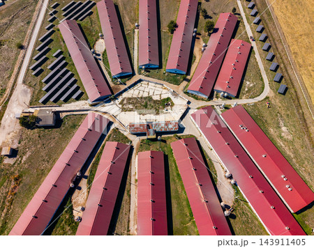 Aerial view of long red-roofed farm buildings arranged around a central yard with rows of solar panels nearby 143911405