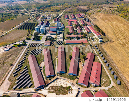 Aerial view of a poultry farm with long barns, grain silos, and service buildings surrounded by fields Aerial view of a poultry farm with long barns, grain silos, and service buildings surrounded by fields 143911406
