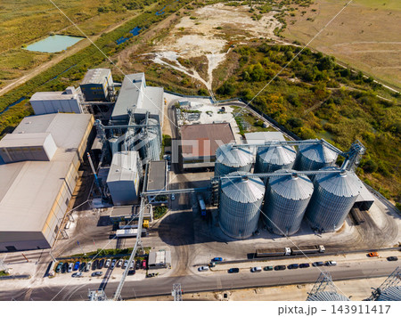 Aerial view of an industrial grain processing facility with storage silos beside a road and open land 143911417