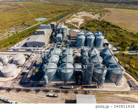 Aerial view of an industrial grain storage and processing facility beside rail tracks in a rural area Aerial view of an industrial grain storage and processing facility beside rail tracks in a rural area 143911418