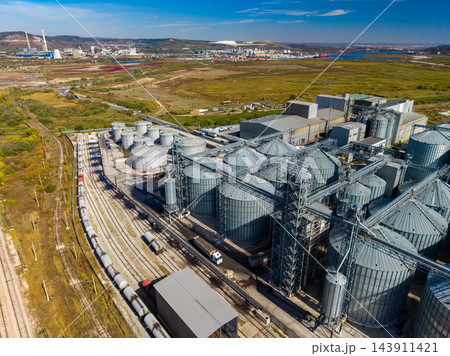 Grain storage silos and freight trains at an industrial port facility in a rural landscape during daylight 143911421