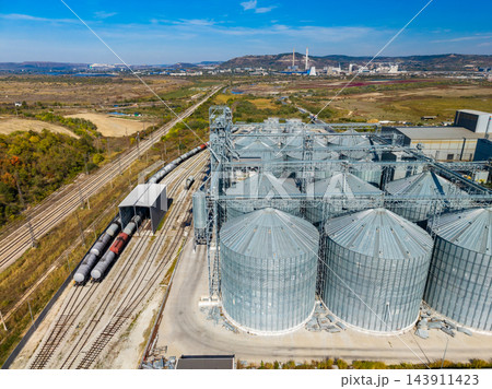 Grain storage silos and freight train beside railway tracks at an industrial facility during the day Grain storage silos and freight train beside railway tracks at an industrial facility during the day 143911423