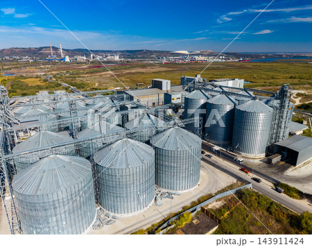 Grain storage silos and processing equipment at an industrial facility near the coast in daylight 143911424