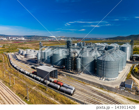 Grain storage silos and rail lines at an industrial facility in a rural landscape during the day Grain storage silos and rail lines at an industrial facility in a rural landscape during the day 143911426
