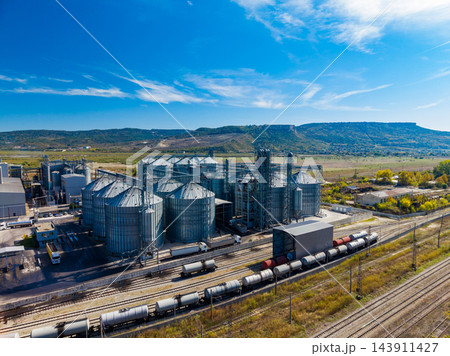 Grain silos and freight trains at an industrial rail facility in a rural landscape under a blue sky 143911427