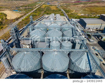 Aerial view of grain storage silos and processing equipment at an industrial facility beside rail tracks 143911443