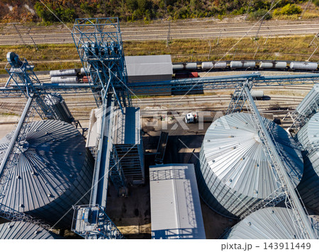 Grain silos and conveyor equipment beside freight rail tracks at an agricultural storage facility in daylight 143911449