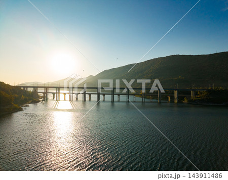 Sunset light reflects across a river beneath a road bridge with hills in the background Sunset light reflects across a river beneath a road bridge with hills in the background 143911486