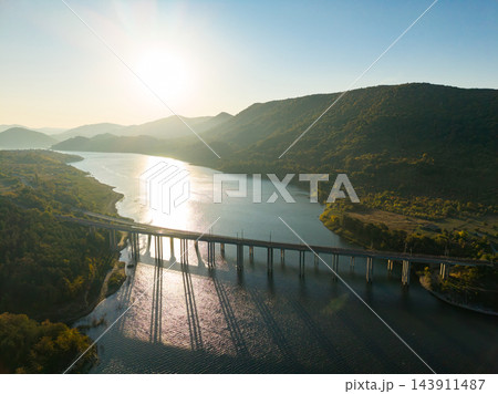 Sunlight reflects across a river beneath a road bridge in a mountain valley at sunset Sunlight reflects across a river beneath a road bridge in a mountain valley at sunset 143911487