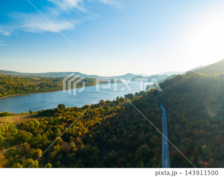 Road winding through forested hills beside a river in a mountain valley during the day Road winding through forested hills beside a river in a mountain valley during the day 143911500