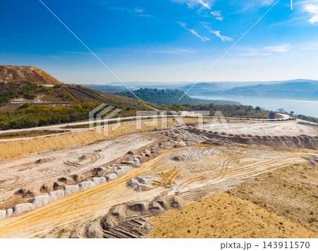 Terraced excavation site on a hillside above a distant lake under a blue sky during daytime Terraced excavation site on a hillside above a distant lake under a blue sky during daytime 143911570