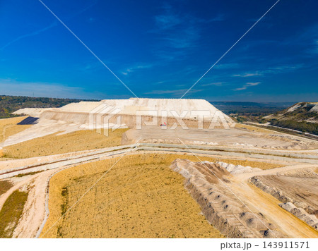 Terraced earthworks and pale mineral deposits spread across an open quarry beneath a blue sky 143911571