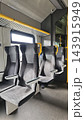 Empty modern public train seats with patterned upholstery, gray flooring, yellow handrails, bright window, and sleek interior fixtures inside a contemporary passenger rail carriage 143915949