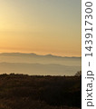 夕焼けに染まる山並みと草原のシルエット 143917300