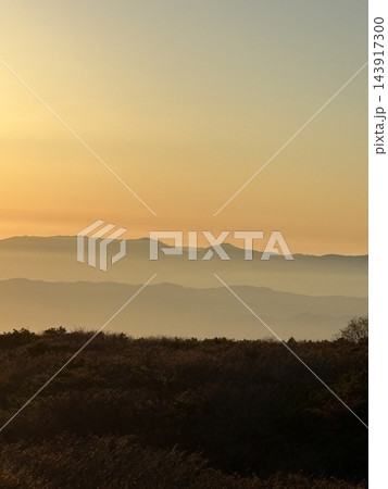 夕焼けに染まる山並みと草原のシルエット 143917300