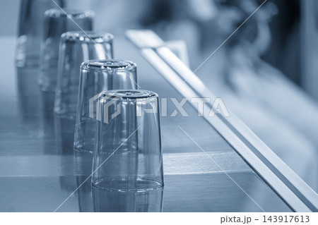 Row of plastic glasses on a conveyor belt after the injection molding process in a blue tone scene 143917613