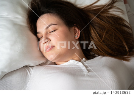 Woman resting with eyes closed on a white pillow in bed at home. Sleep quality comfortable bedding and restorative wellness 143918652