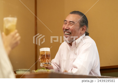 居酒屋で生ビールを飲む笑顔のシニア男性 143919581