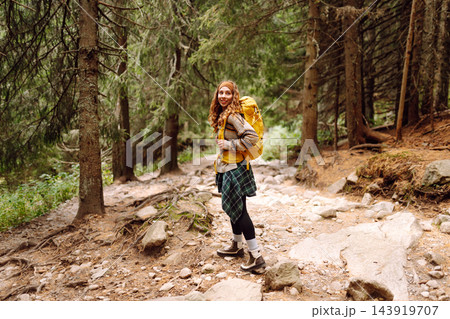 A person walks on a forest trail with a yellow backpack. Trees line both sides of the path. 143919707