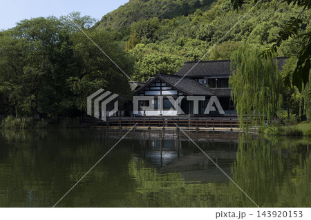 Traditional Asian style architecture building reflected in a serene lake surrounded by a lush green forest on a bright day Traditional Asian style architecture building reflected in a serene lake surrounded by a lush green forest on a bright day 143920153