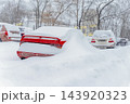 Red Car Buried Under Deep Snow. Heavy Winter Snowfall. Bright car remains buried under snow in parking lot, severe winter weather. Heavy snow covers car, transportation disruption, extreme cold 143920323