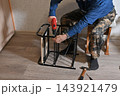 Man fixes wooden chair in a home setting with a plant nearby 143921479