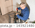Man using power drill to assemble furniture in home setting during daytime 143921480