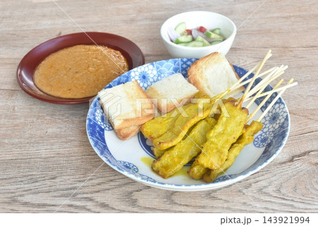 grilled pork satay stabing wooden stick couple bread dipping with sweet peanut sauce and pickled vegetable Indonesian food on plate grilled pork satay stabing wooden stick couple bread dipping with sweet peanut sauce and pickled vegetable Indonesian food on plate 143921994