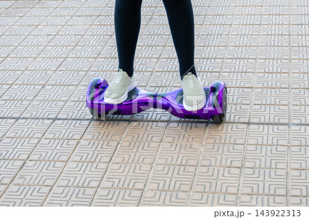 Girl in sneakers riding the violet hoverboard on the brick road. New technologies. Self balancing electric smart skateboard. Electrical scooter for play outside. 143922313